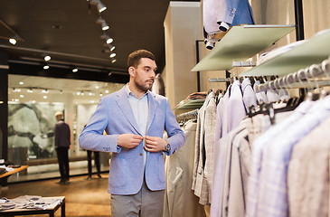 Image showing happy young man trying jacket on in clothing store