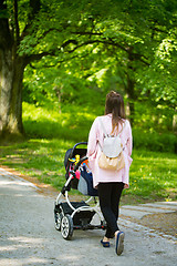 Image showing Happy mother walking with baby stroller in park