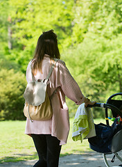 Image showing Happy mother walking with baby stroller in park