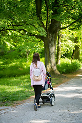 Image showing Happy mother walking with baby stroller in park