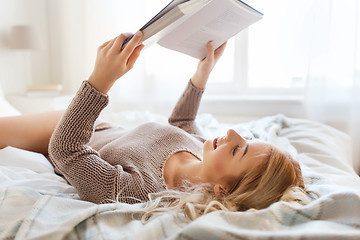 Image showing young woman reading book in bed at home