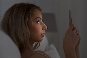 Image showing young woman with smartphone in bed at night