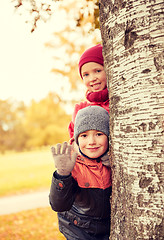 Image showing happy children hiding behind tree and waving hand