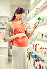 Image showing happy pregnant woman choosing lotion at pharmacy