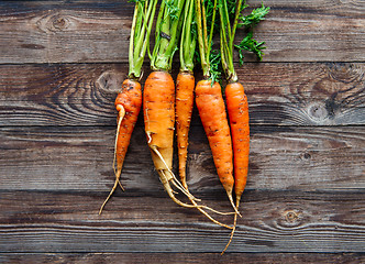 Image showing Raw carrot with green leaves on wooden background