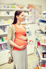 Image showing happy pregnant woman choosing medicine at pharmacy