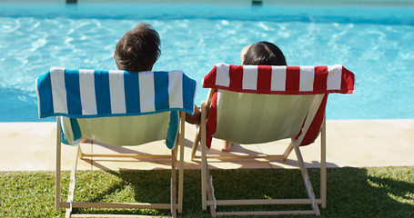 Image showing Couple relaxing in colorful deck chairs poolside