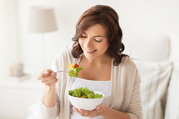 Image showing smiling young woman eating salad at home