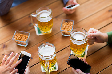 Image showing close up of hands with smartphones and beer at bar