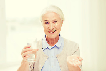 Image showing happy senior woman with water and medicine at home