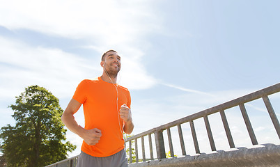 Image showing happy man with earphones running outdoors