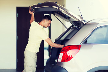 Image showing young man with open car trunk at parking space