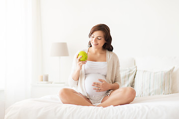 Image showing happy pregnant woman eating green apple at home