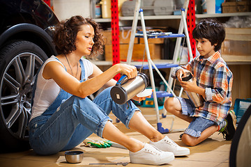 Image showing Mechanic woman pours tea from a thermos into a cup for the child