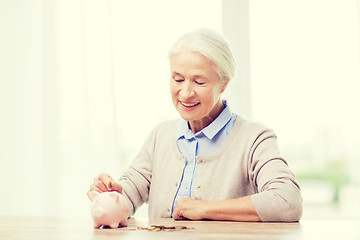 Image showing senior woman putting money to piggy bank at home