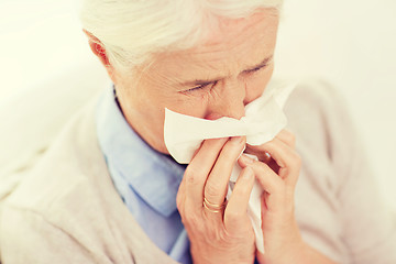 Image showing sick senior woman blowing nose to paper napkin