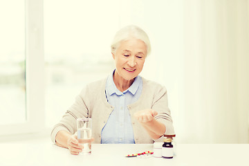 Image showing happy senior woman with water and medicine at home