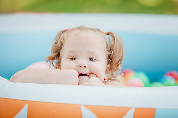 Image showing The little baby girl playing with toys in inflatable pool in the summer sunny day