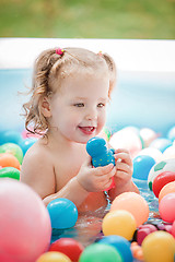 Image showing The little baby girl playing with toys in inflatable pool in the summer sunny day