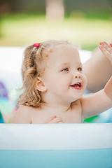 Image showing The little baby girl playing with toys in inflatable pool in the summer sunny day