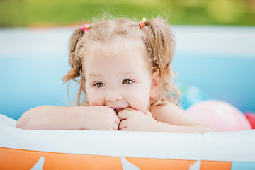 Image showing The little baby girl playing with toys in inflatable pool in the summer sunny day