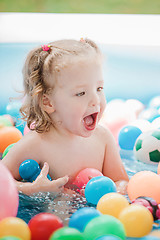 Image showing The little baby girl playing with toys in inflatable pool in the summer sunny day