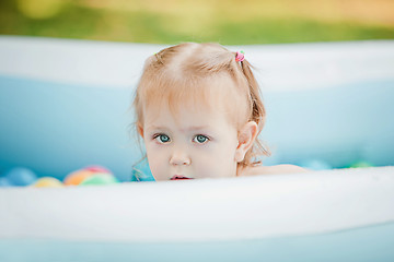 Image showing The little baby girl playing with toys in inflatable pool in the summer sunny day