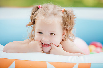 Image showing The little baby girl playing with toys in inflatable pool in the summer sunny day