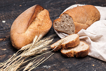 Image showing Rustic bread on wood table. Dark wooden background