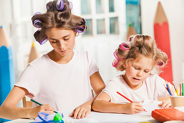 Image showing The young mother and her little daughter drawing with pencils at home