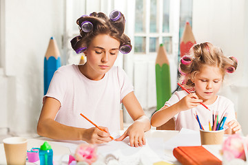 Image showing The young mother and her little daughter drawing with pencils at home