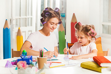 Image showing The young mother and her little daughter drawing with pencils at home