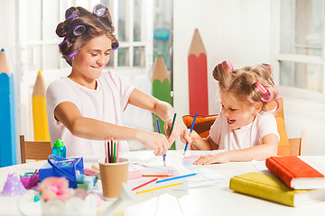 Image showing The young mother and her little daughter drawing with pencils at home