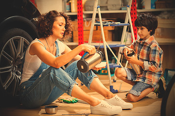 Image showing Mechanic woman pours tea from a thermos into a cup for the child