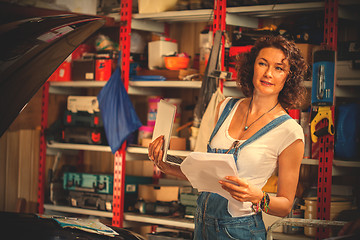 Image showing woman mechanic in blue denim overalls with a laptop and sheets o