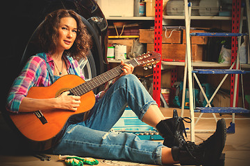 Image showing beautiful Woman mechanic in blue overalls resting with a guitar