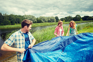 Image showing group of smiling friends setting up tent outdoors