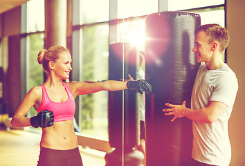 Image showing smiling woman with personal trainer boxing in gym