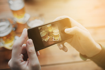 Image showing close up of hands with smartphone picturing beer