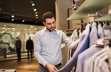 Image showing happy young man choosing clothes in clothing store