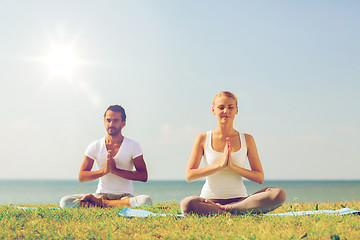 Image showing smiling couple making yoga exercises outdoors