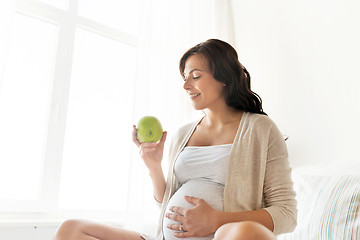 Image showing happy pregnant woman eating green apple at home