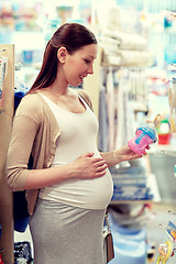Image showing happy pregnant woman choosing baby bottle at shop