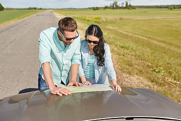 Image showing happy man and woman with road map on car hood