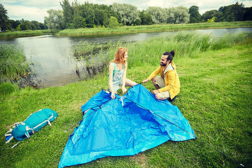 Image showing happy couple setting up tent outdoors