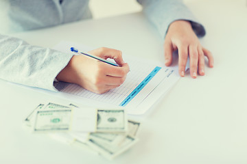 Image showing close up of hands with money filling tax form