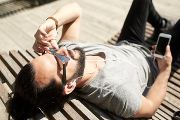 Image showing man with earphones and smartphone on city bench