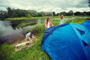 Image showing group of smiling friends setting up tent outdoors