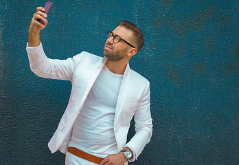 Image showing Young man in white clothes taking selfie, stylish portrait