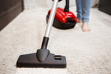 Image showing Woman doing cleaning in room, vacuuming white carpet. Image of female foot, red vacuum cleaner and black head of vacuum cleaner closeup